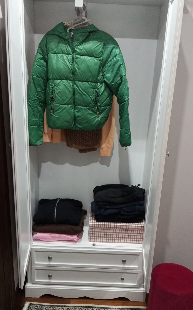 Armadio in legno bianco stile Arte Povera, organizzato con vestiti appesi e abbigliamento piegato sui ripiani.