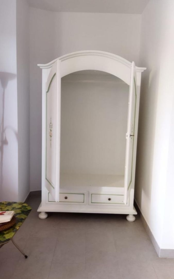 Armadio bianco a due ante aperto, stile provenzale con decori e cassetti inferiori.