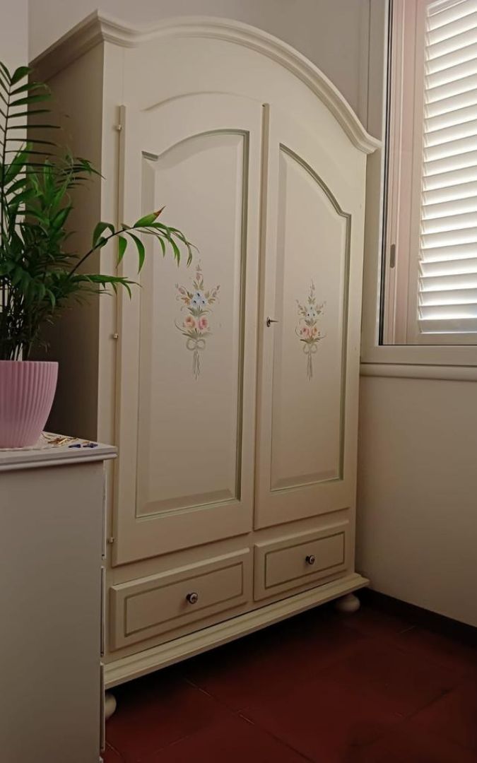 Armadio in legno bianco con finiture decorate posizionato in una stanza luminosa.