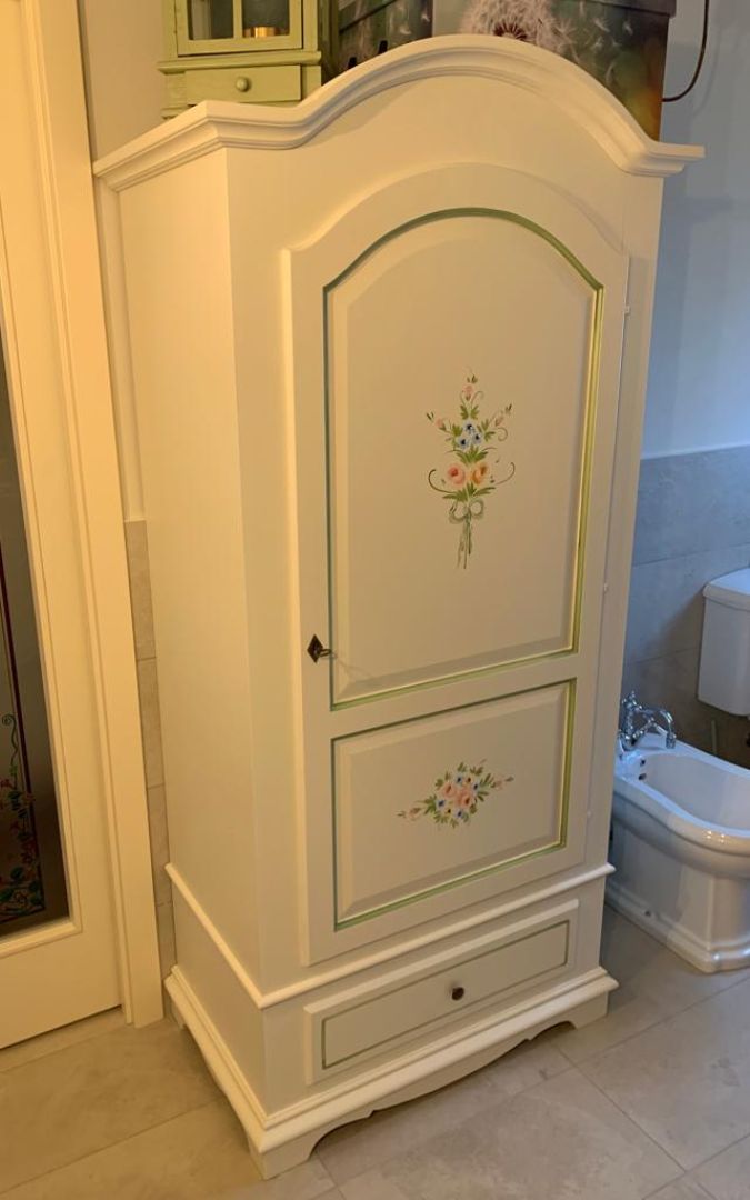 Armadio singolo bianco con decorazioni floreali dipinte a mano e un cassetto inferiore.