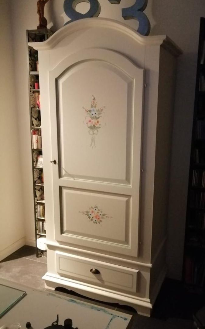 Armadio a una anta con decorazioni floreali bianche e perla su fondo bianco opaco.