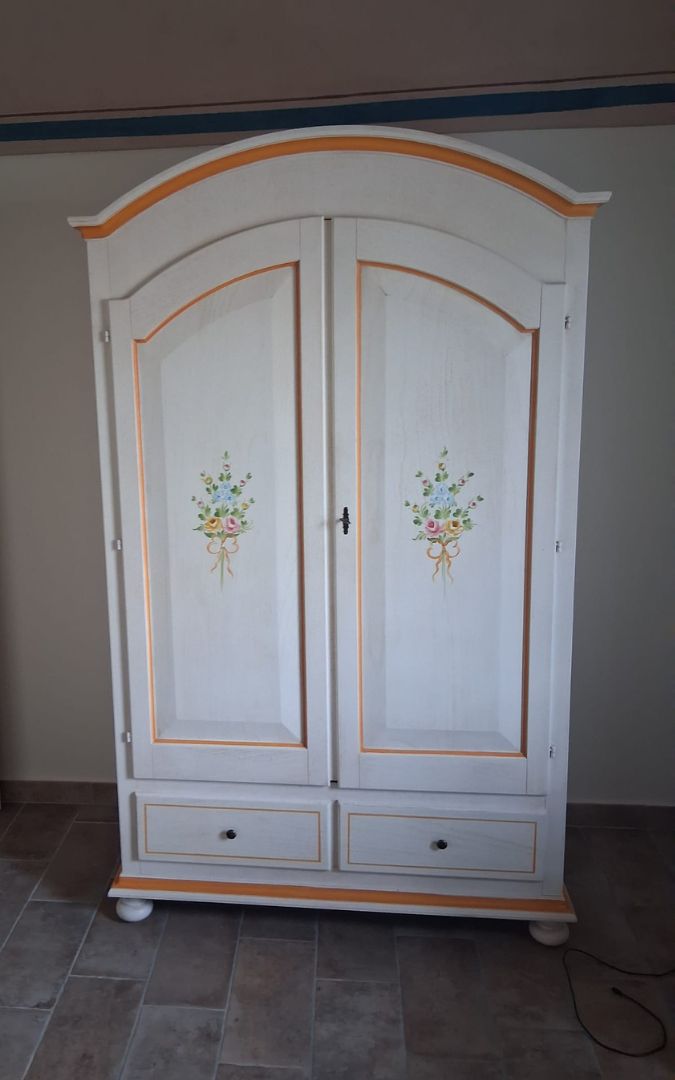Armadio in legno bianco stile Arte Povera con decorazioni floreali dipinte a mano e finiture color ocra.