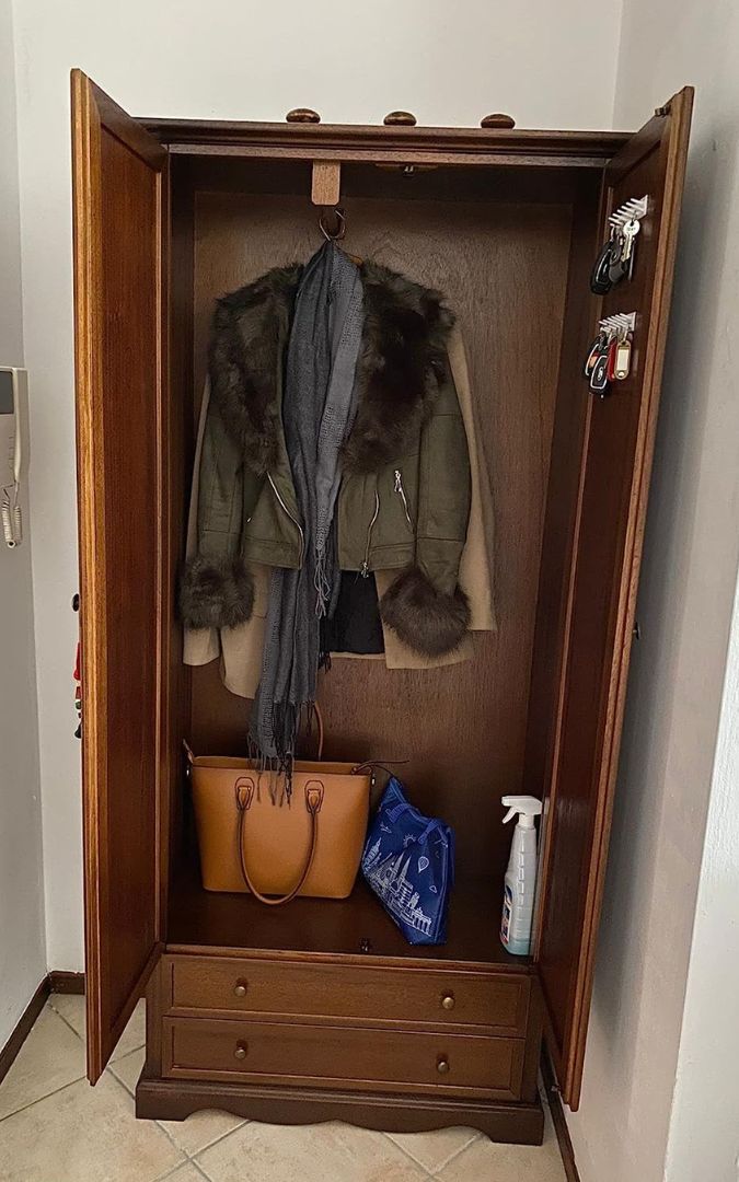 Interno di un armadio in legno noce scuro con appendiabiti, giacca e borsa, due cassetti inferiori visibili.