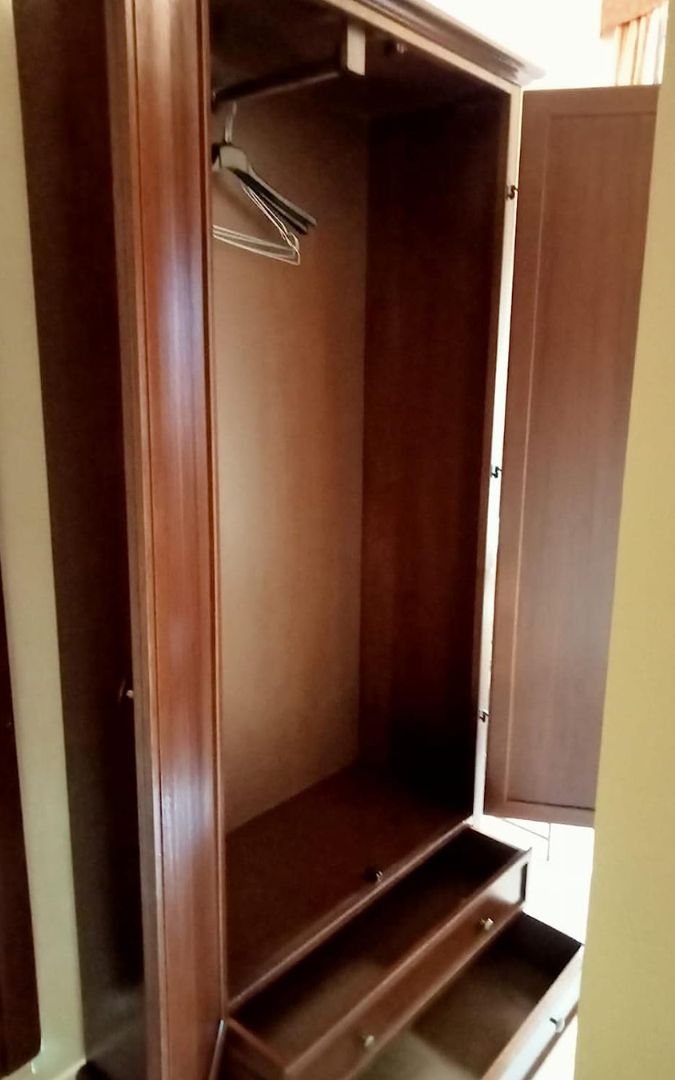 Vista angolare di un armadio in legno noce scuro, due ante e due cassetti, design Arte Povera.