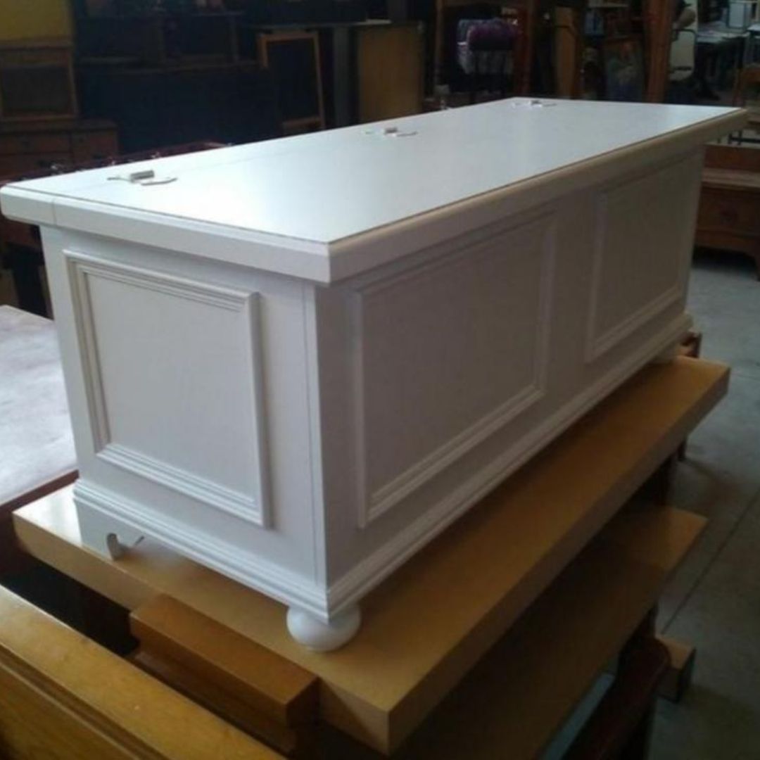Cassapanca in legno bianco posizionata su una base in officina, vista angolare con cerniere superiori.