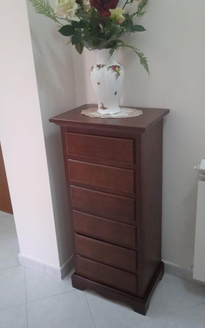 Cassettiera in legno noce scuro a sei cassetti posta accanto a una poltrona classica.