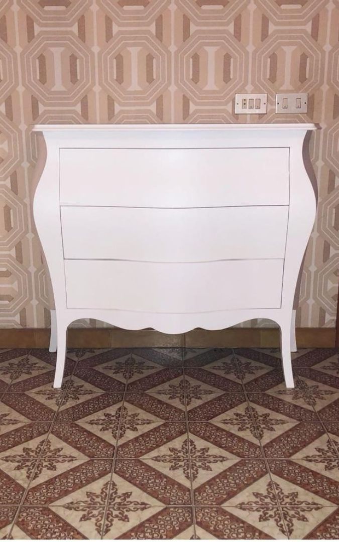 Comò bianco a 3 cassetti con design curvo, arricchito da specchio decorativo a raggiera e cornici fotografiche su piano
