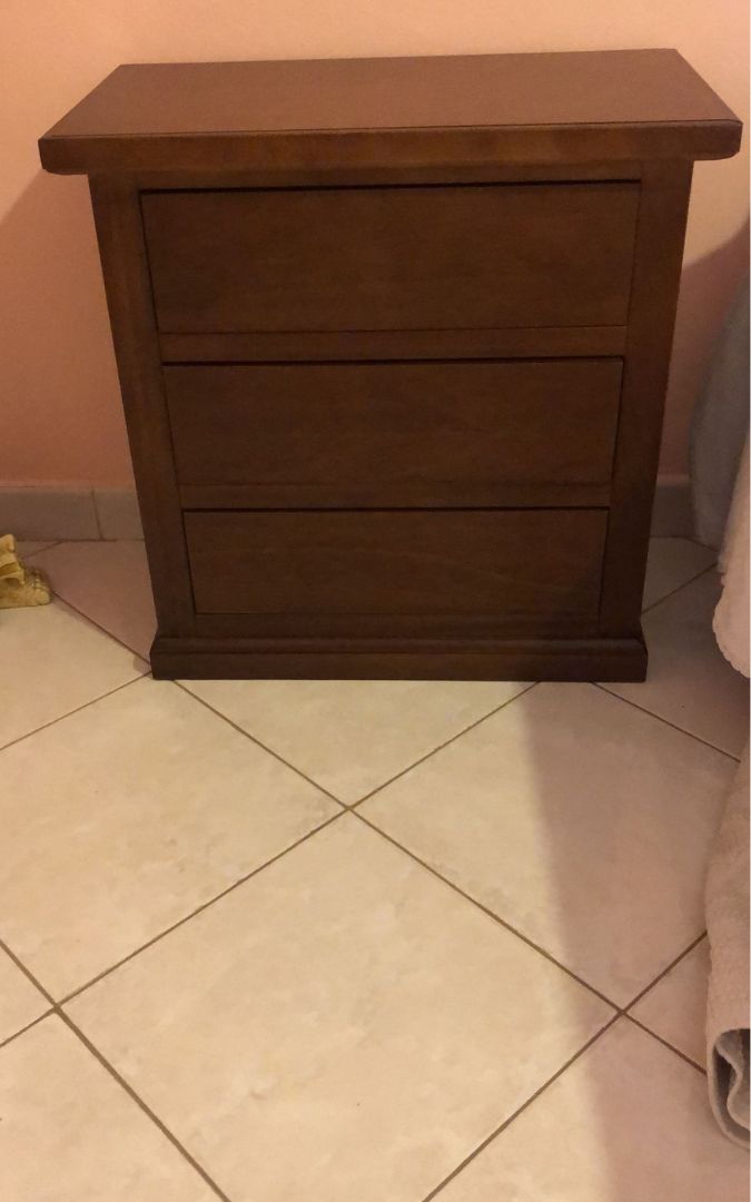 Comodino classico in legno noce scuro dotato di tre cassetti, ideale per camera da letto.