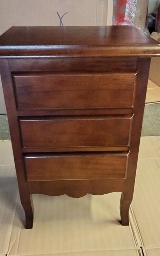 Comodino in legno massello con 3 cassetti, finitura noce scuro, posizionato in un ambiente domestico.