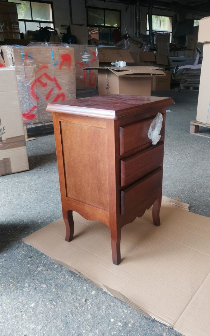 Comodino in legno con 3 cassetti, finitura noce scuro, vista frontale su base di cartone.