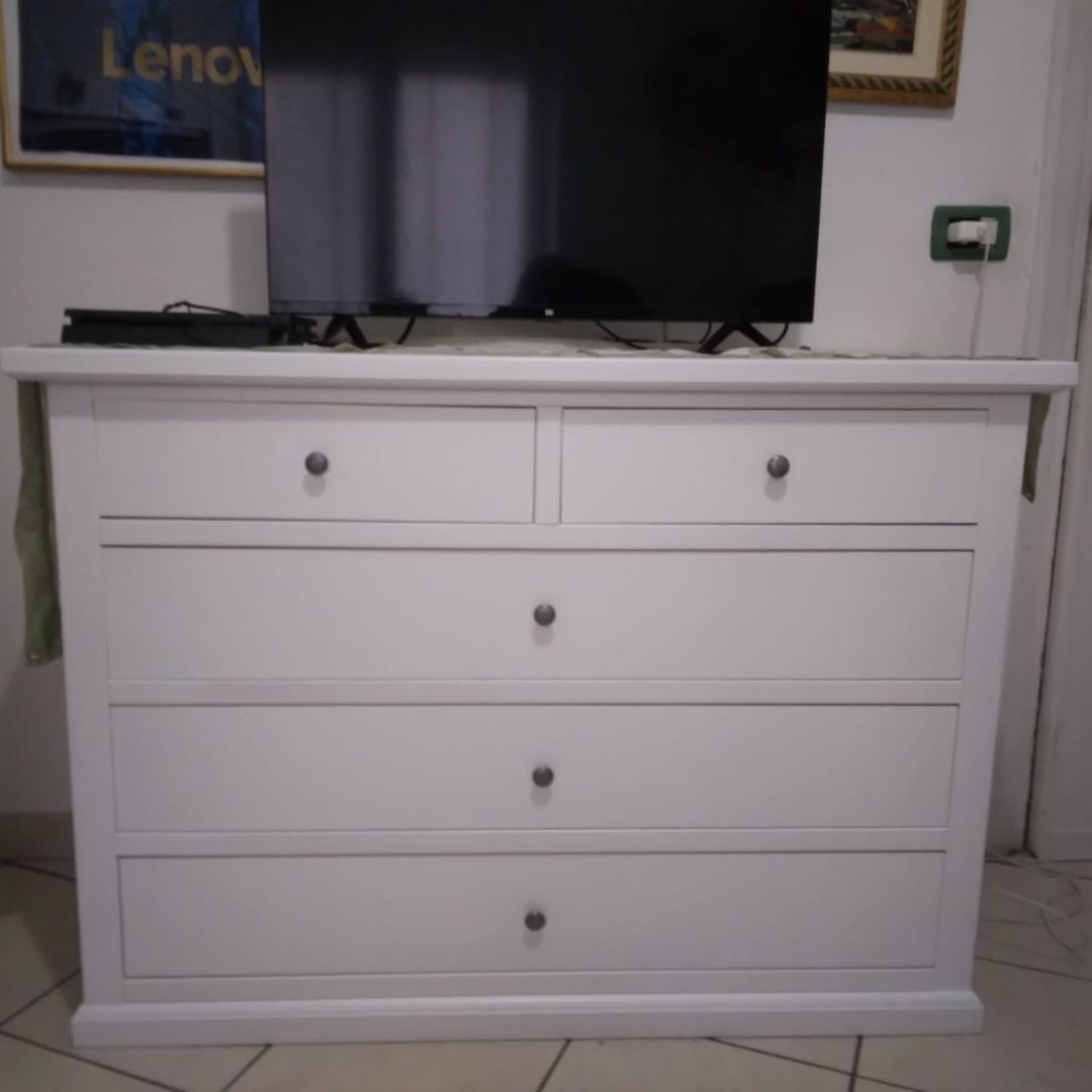 Comò in legno bianco opaco con 5 cassetti, utilizzato come mobile porta-TV in ambiente domestico.