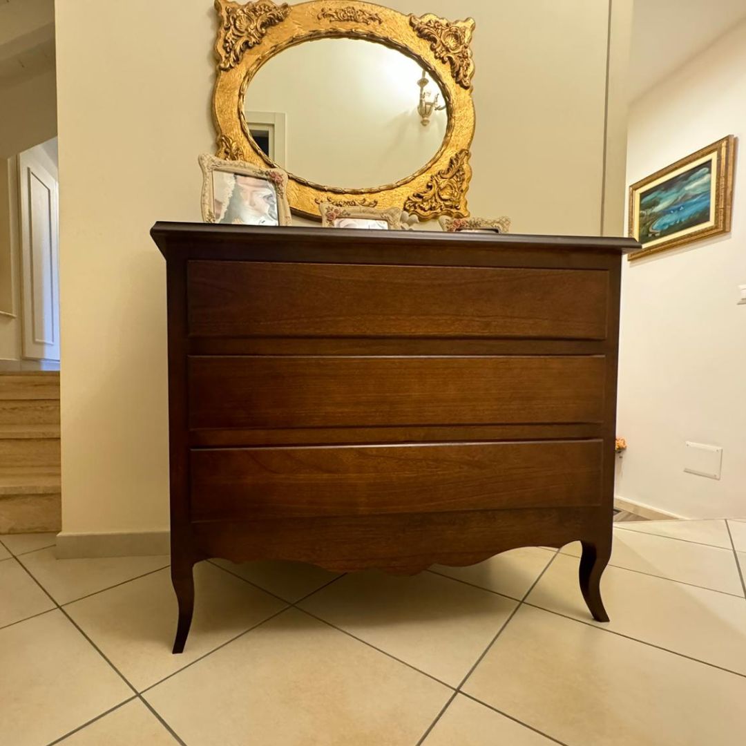 Comò in legno a 3 cassetti stile classico sotto uno specchio dorato decorativo.