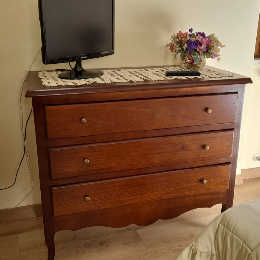 Comò classico in legno finitura noce scuro con tre cassetti, decorato con centrino e fiori.