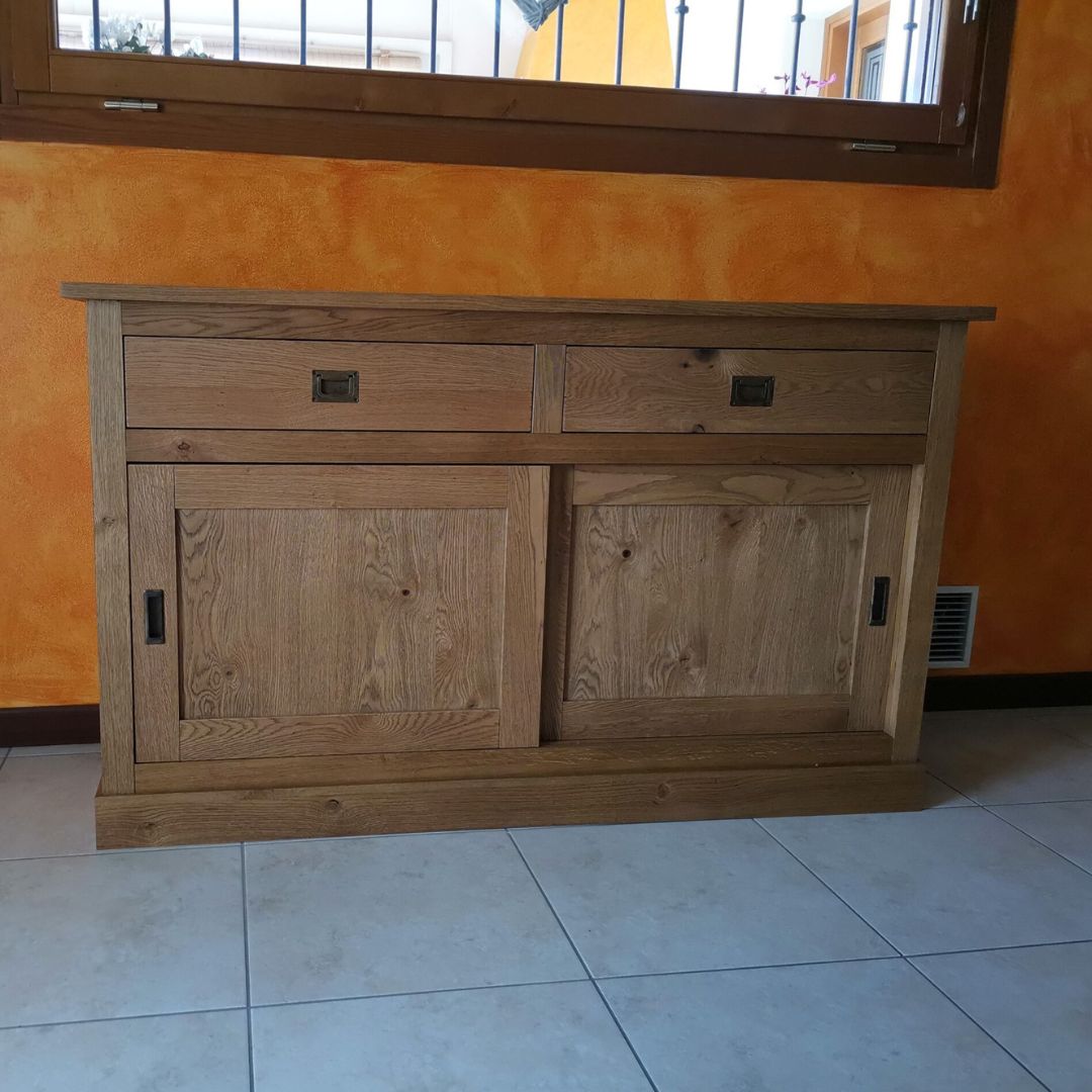Credenza buffet in rovere nodato con due ante scorrevoli e due cassetti, vista frontale su parete arancione.