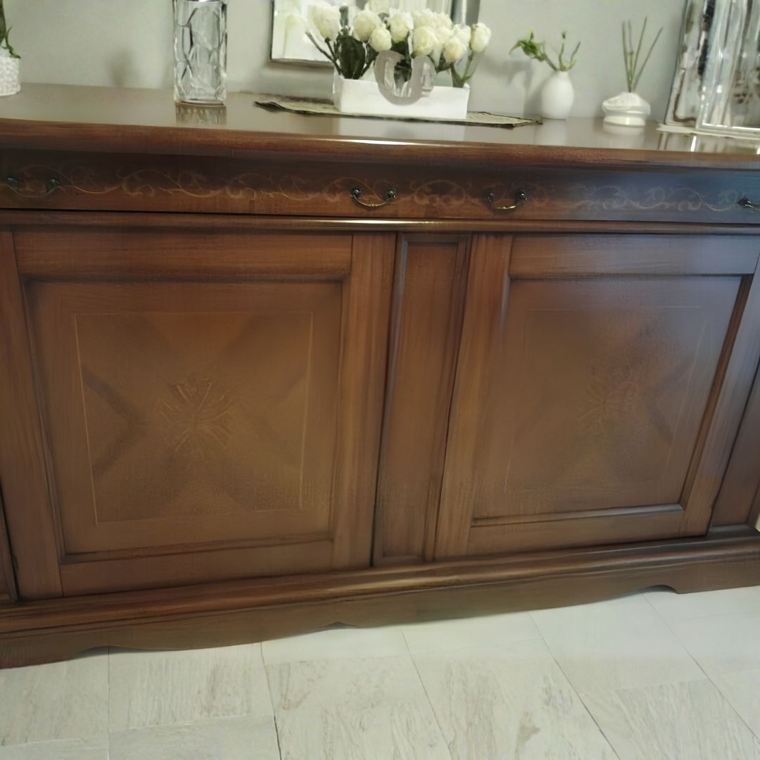 Dettaglio frontale di una credenza madia in legno scuro con intarsi artistici e maniglie classiche, design tradizionale.