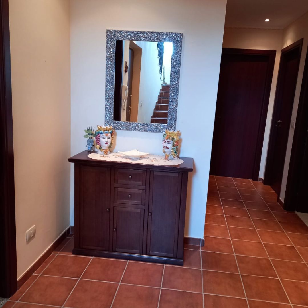 Credenza stile arte povera in legno di pioppo noce scuro con tre ante e due cassetti, collocata in un ingresso sotto uno specchio.