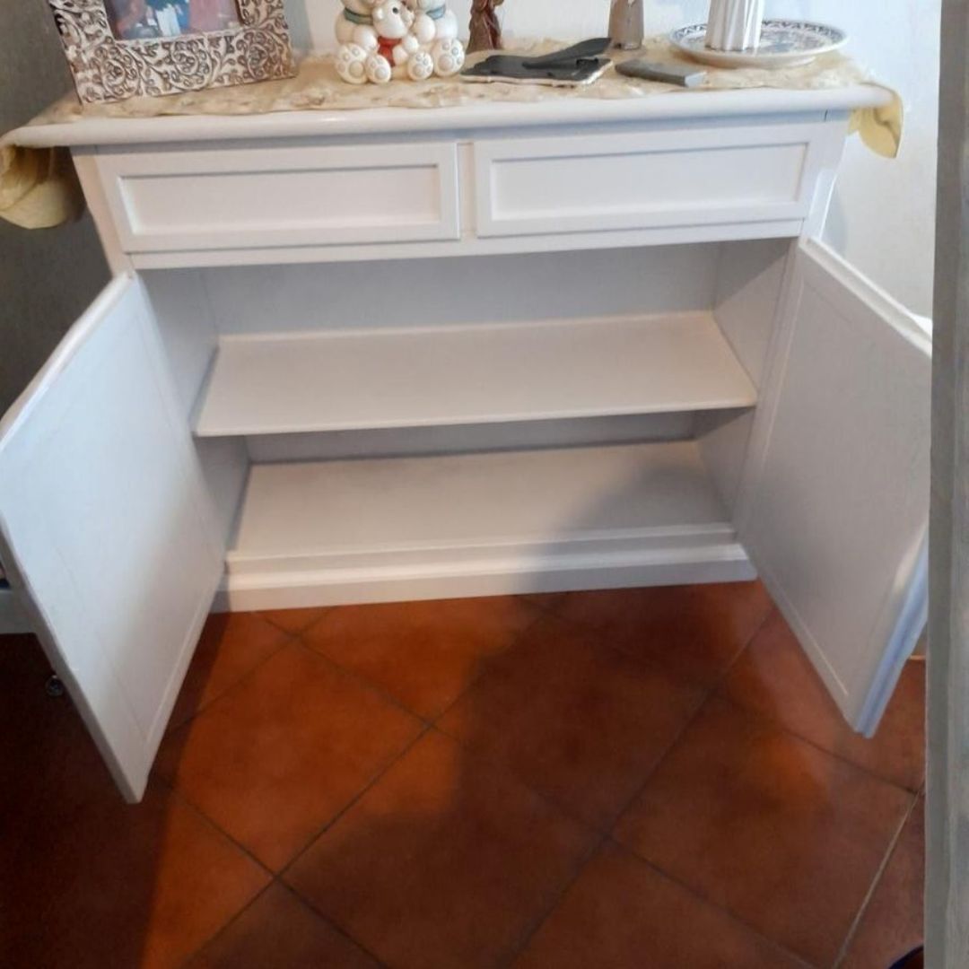 Interno di una credenza in legno bianco con ripiano centrale, mostrata con le ante aperte.