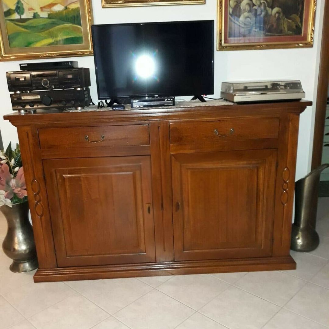 Credenza in legno massello finitura noce stile Arte Povera con due ante e due cassetti, usata come mobile TV.