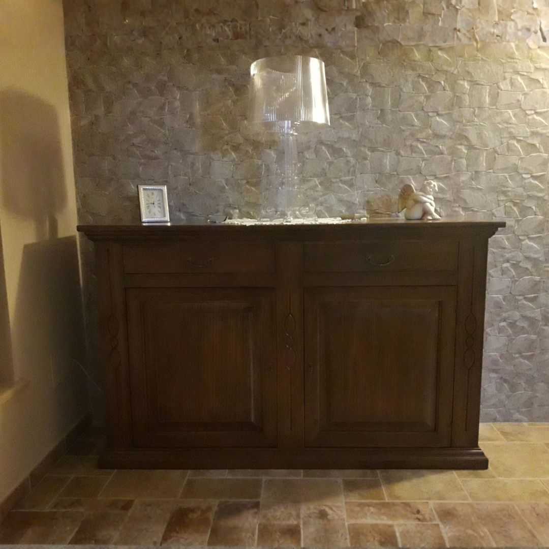 Elegante credenza in legno finitura Bassano, stile classico, posizionata contro una parete in pietra.