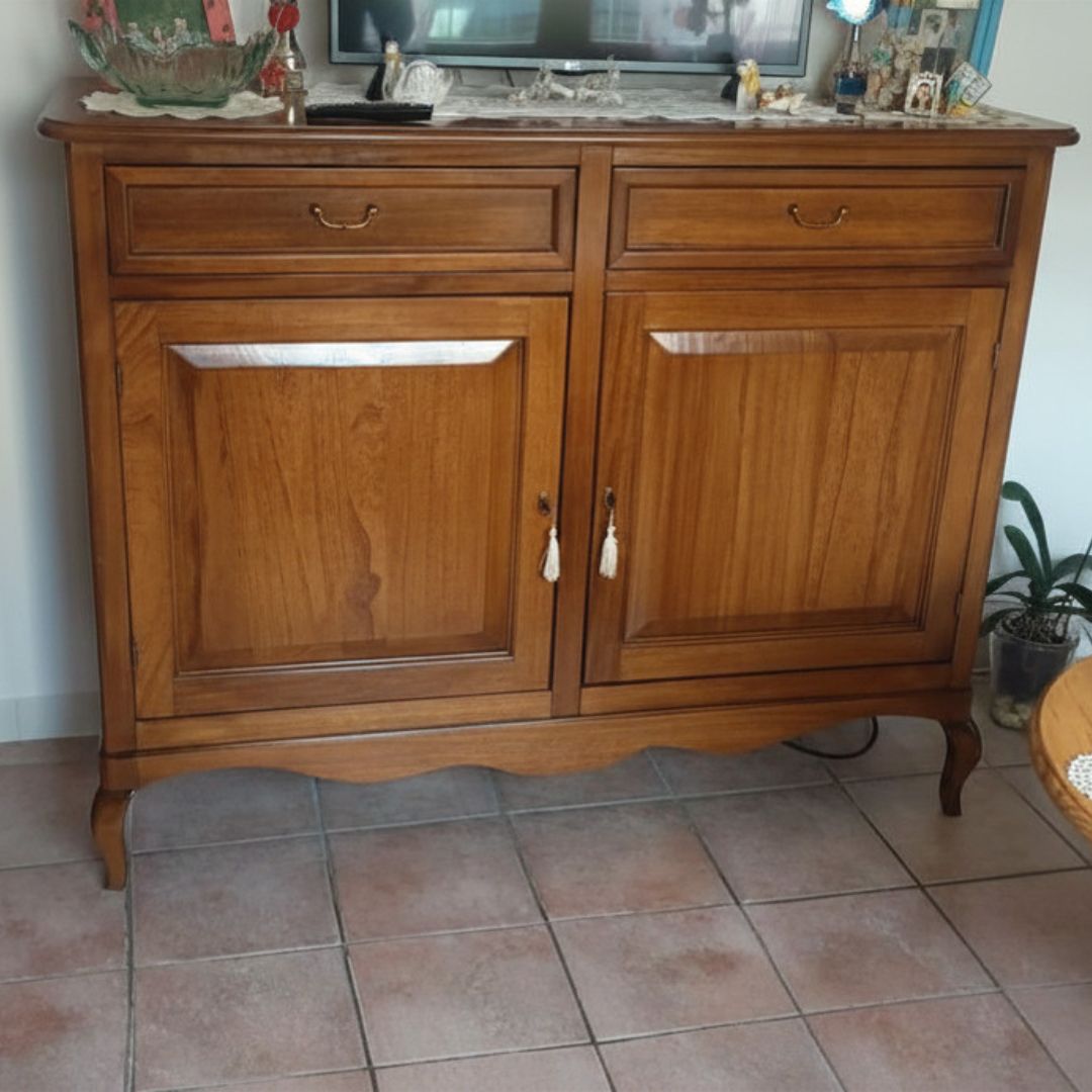 Credenza in legno massello finitura Bassano, stile Arte Povera, con 2 ante e 2 cassetti, posizionata davanti a una finestra con vista panoramica.