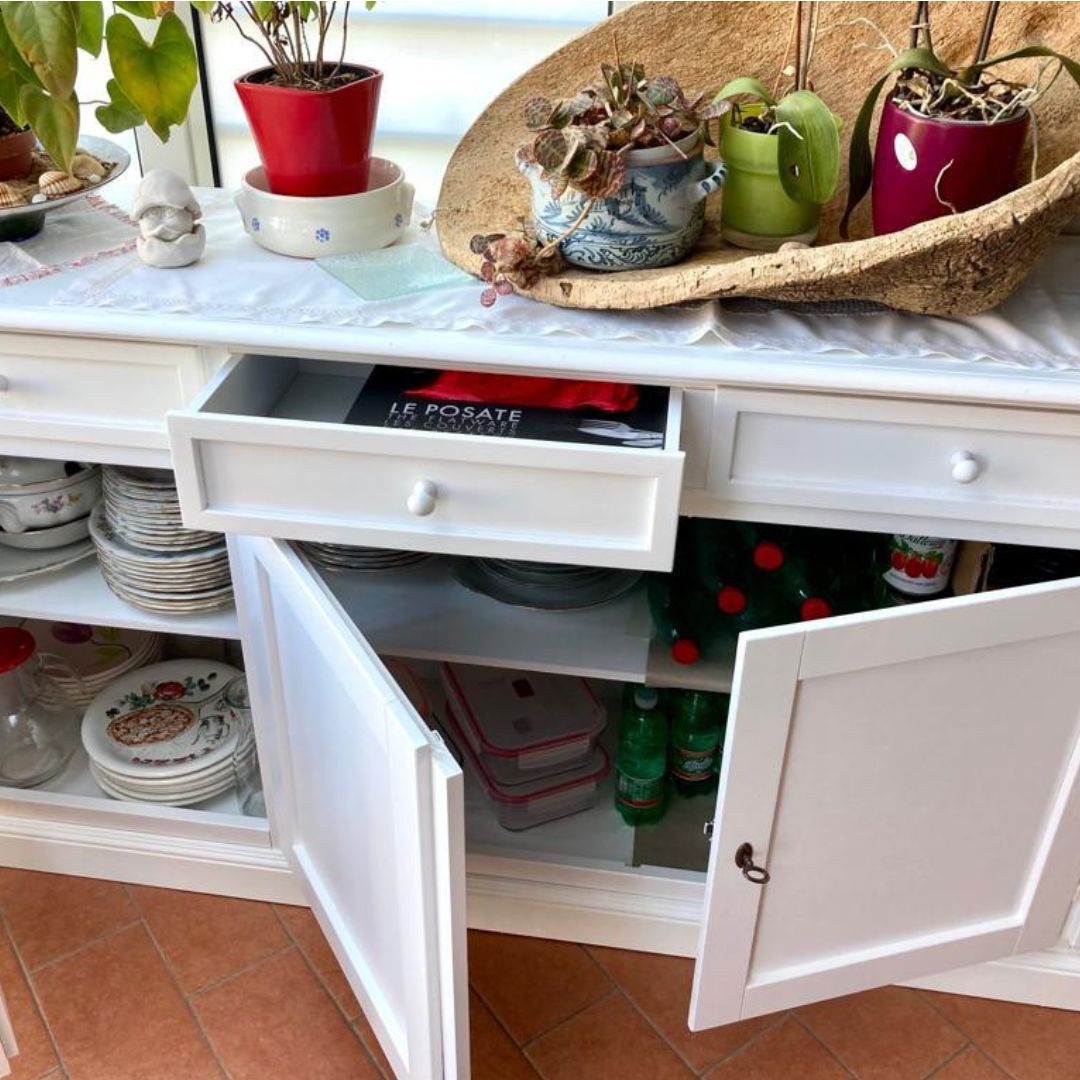 Dettaglio interno di credenza bianca con cassetti e ante aperti.