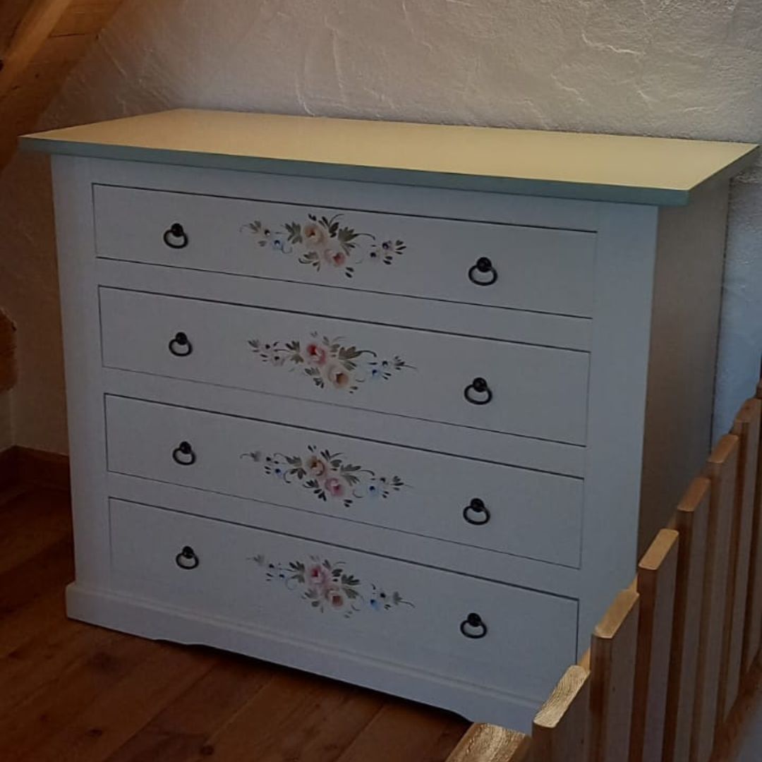 Vista frontale di un comò in legno chiaro con quattro cassetti finemente decorati