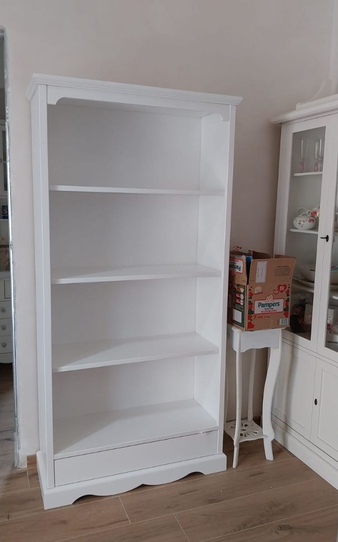 Libreria bianca in stile Arte Povera piena di libri e oggetti decorativi, ideale per arredamento classico.