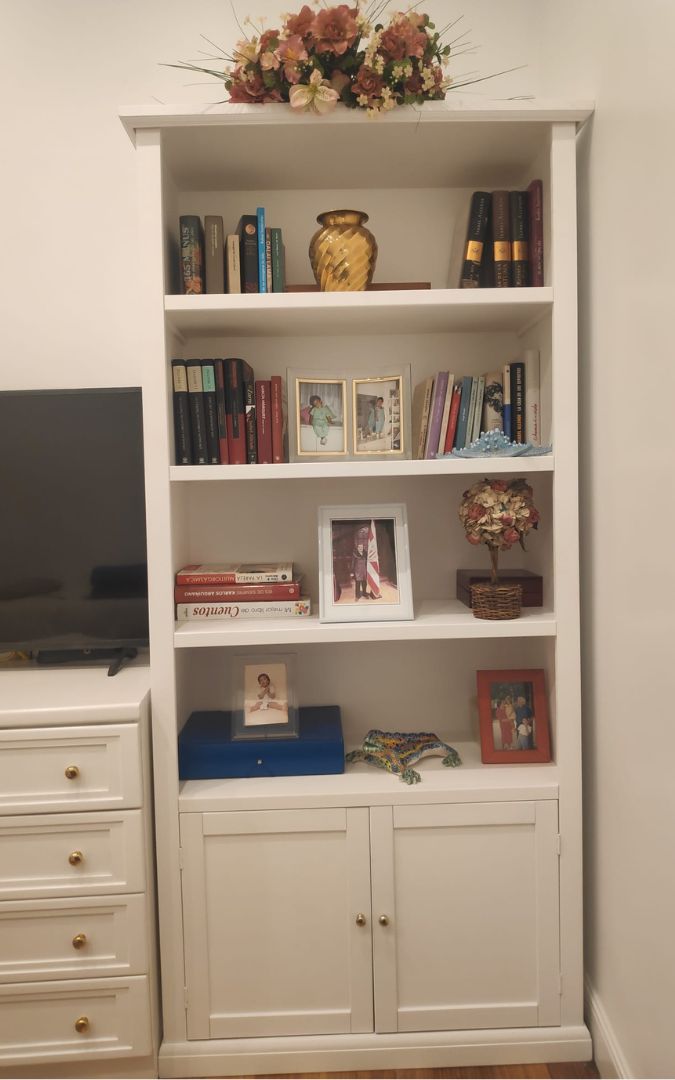 Libreria in legno bianco con decorazioni, libri e cornici, posizionata in un soggiorno in stile classico.