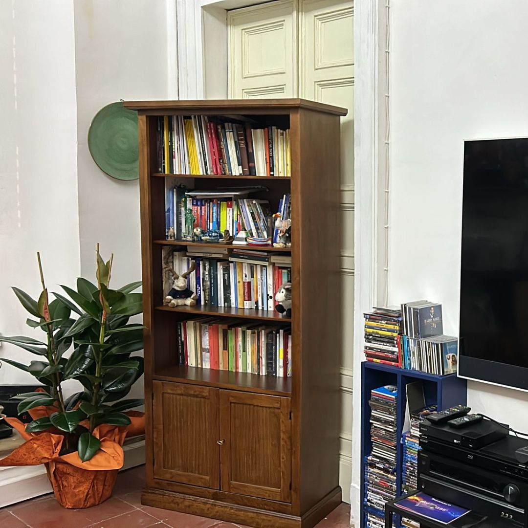 Libreria alta in legno color noce scuro stile arte povera con scaffali a giorno e due ante inferiori.