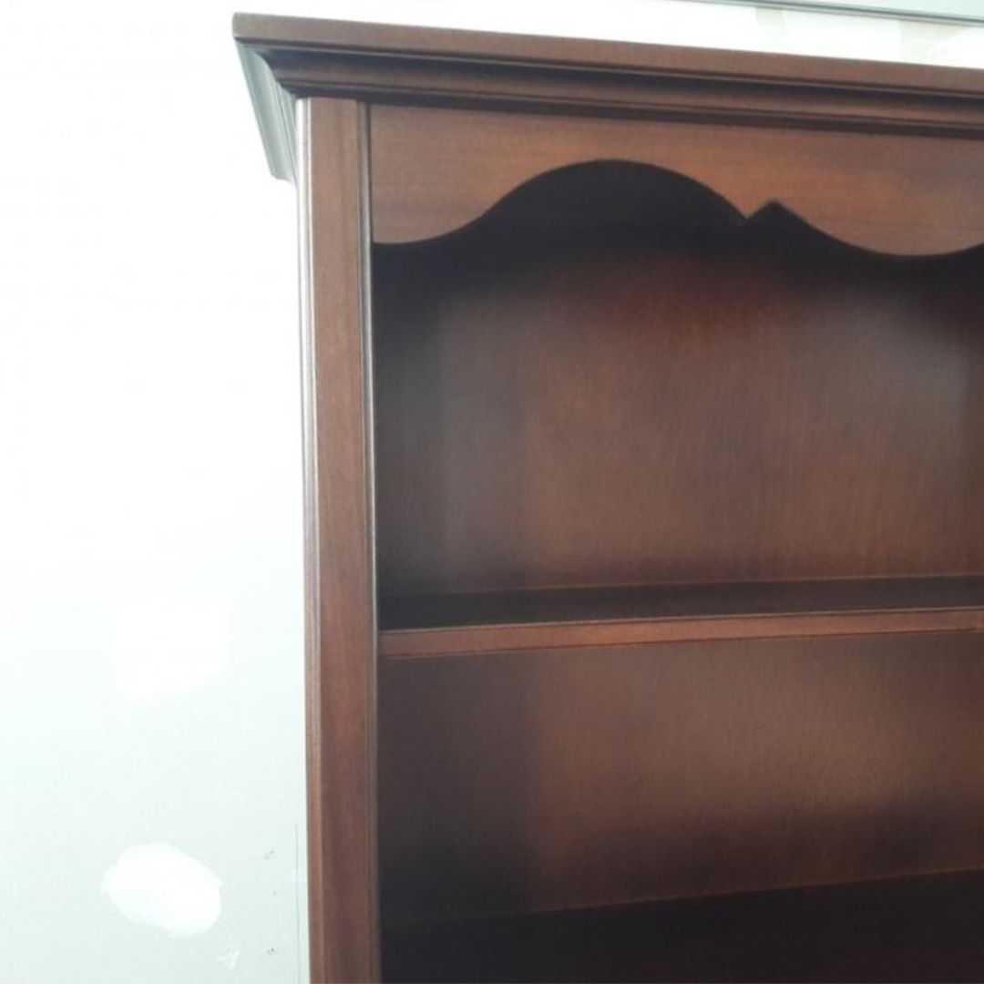 Libreria in legno noce scuro con cinque ripiani riempita di libri e oggetti decorativi.