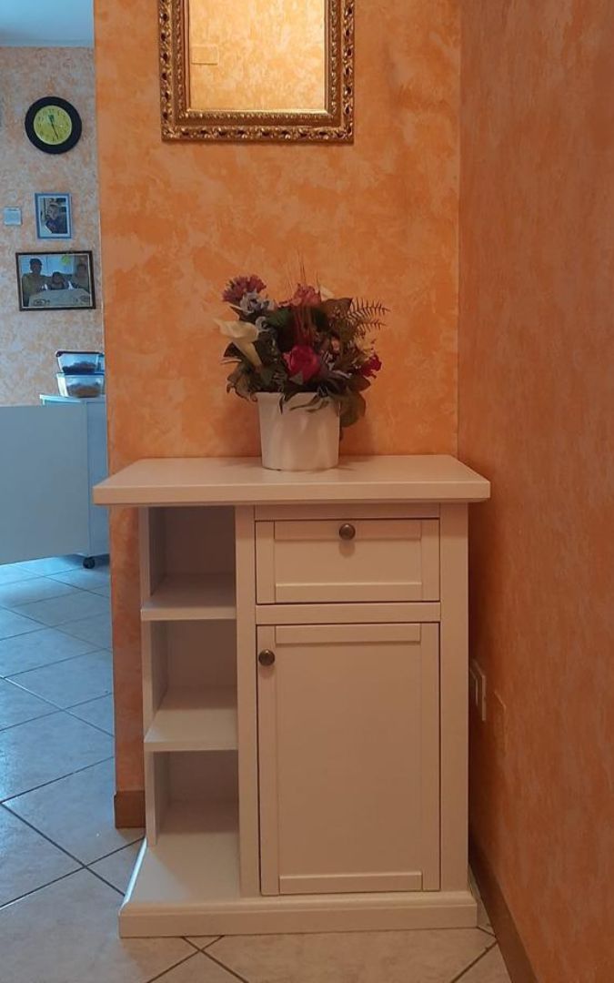Mobile porta telefono in legno bianco opaco, dotato di cassetto, anta e vani a giorno laterali in stile classico.