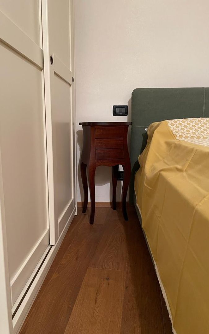 Mobiletto Francesino in legno noce posizionato accanto a un letto, ideale come comodino classico.