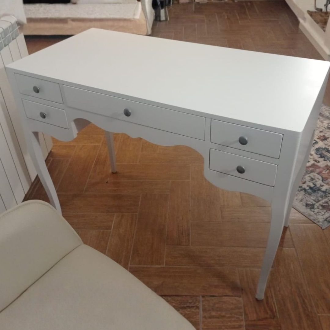 Vista angolare di una scrivania in legno bianco opaco con 5 cassetti e finiture classiche