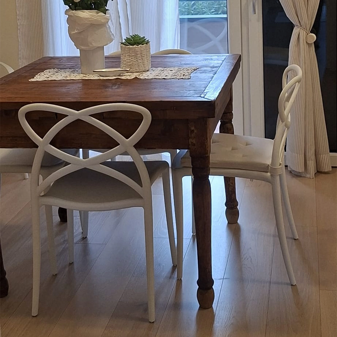 Set di 4 sedie impilabili bianche in polipropilene con schienale intrecciato posizionate attorno a un tavolo in legno per sala da pranzo.