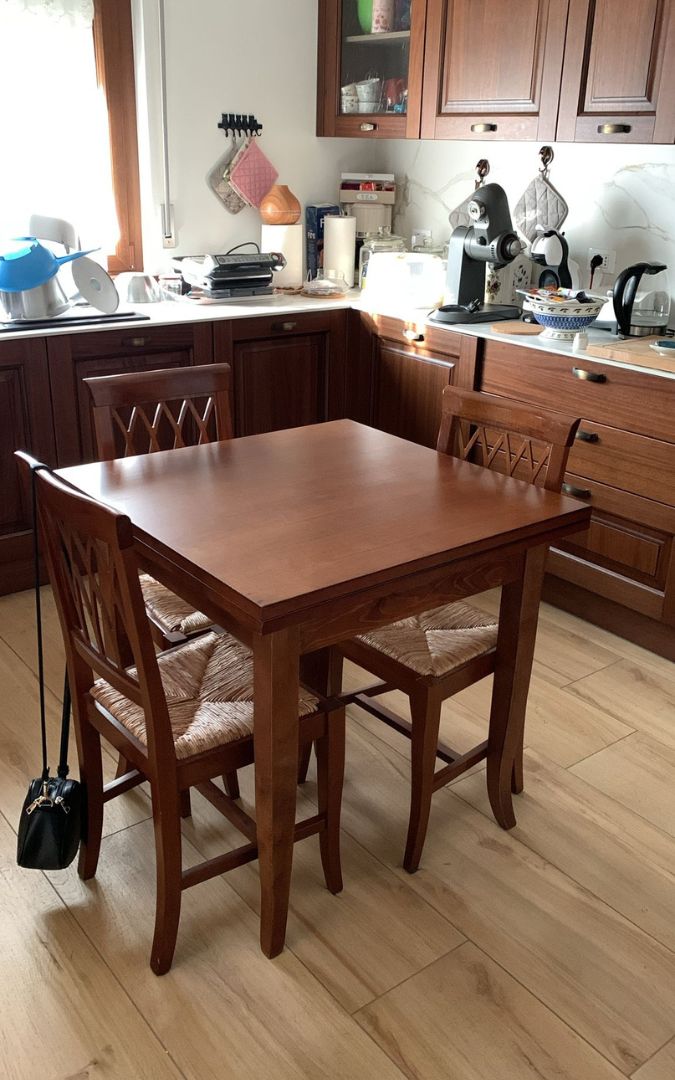 Tavolo allungabile in legno di pioppo color noce scuro con eleganti gambe a sciabola.