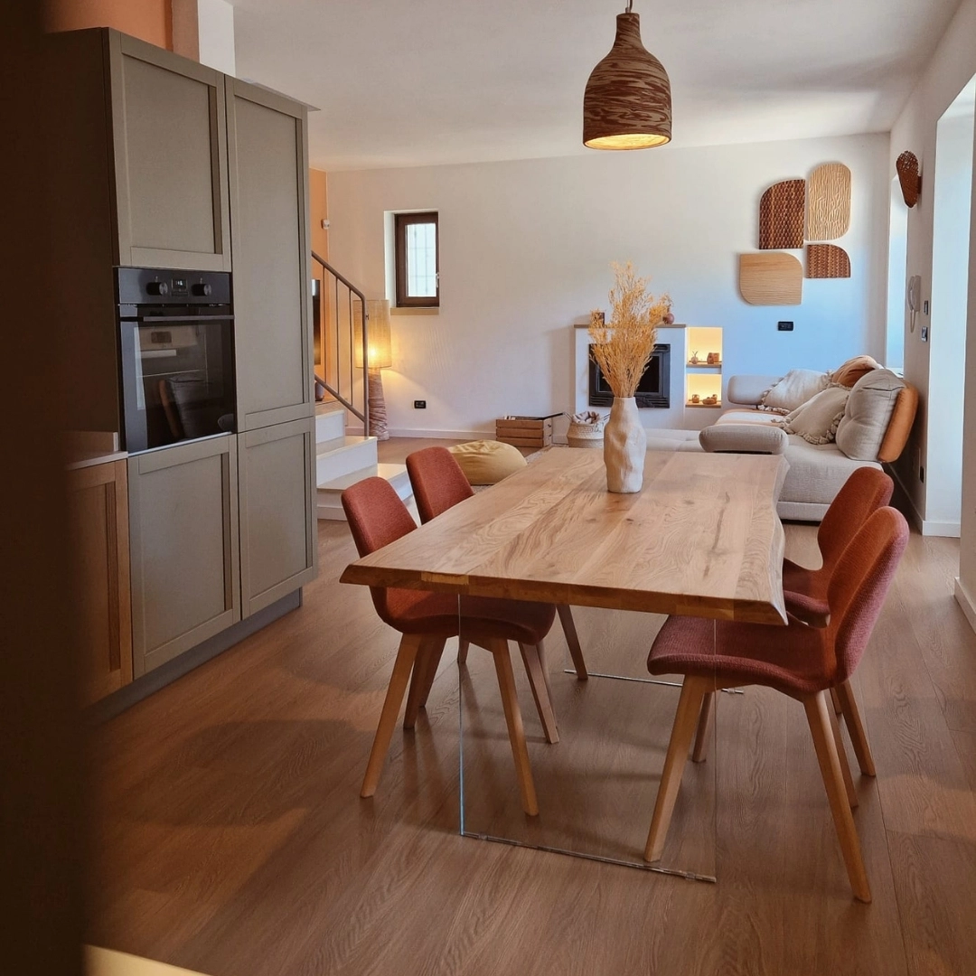 Zona pranzo con tavolo moderno in rovere massello allungabile e gambe in vetro trasparente, sedie in tessuto ruggine