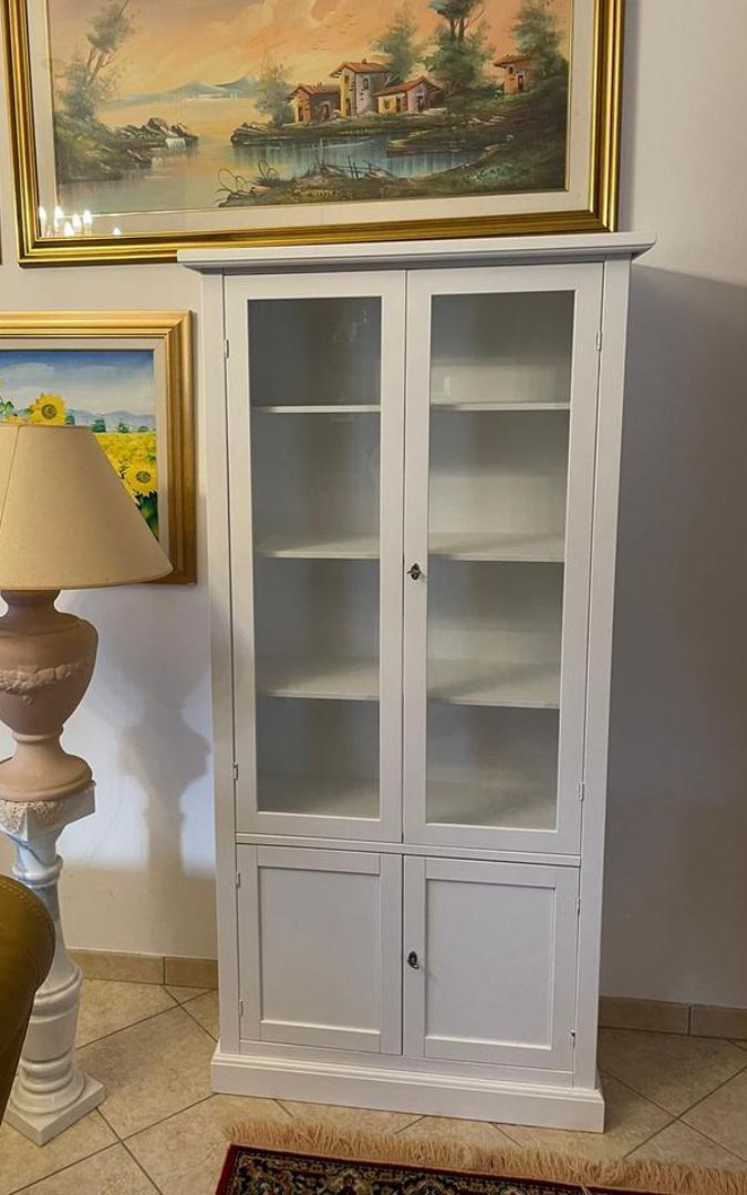 Dettaglio interno di una vetrina in legno bianco opaco con ripiani a vista, stile tradizionale.