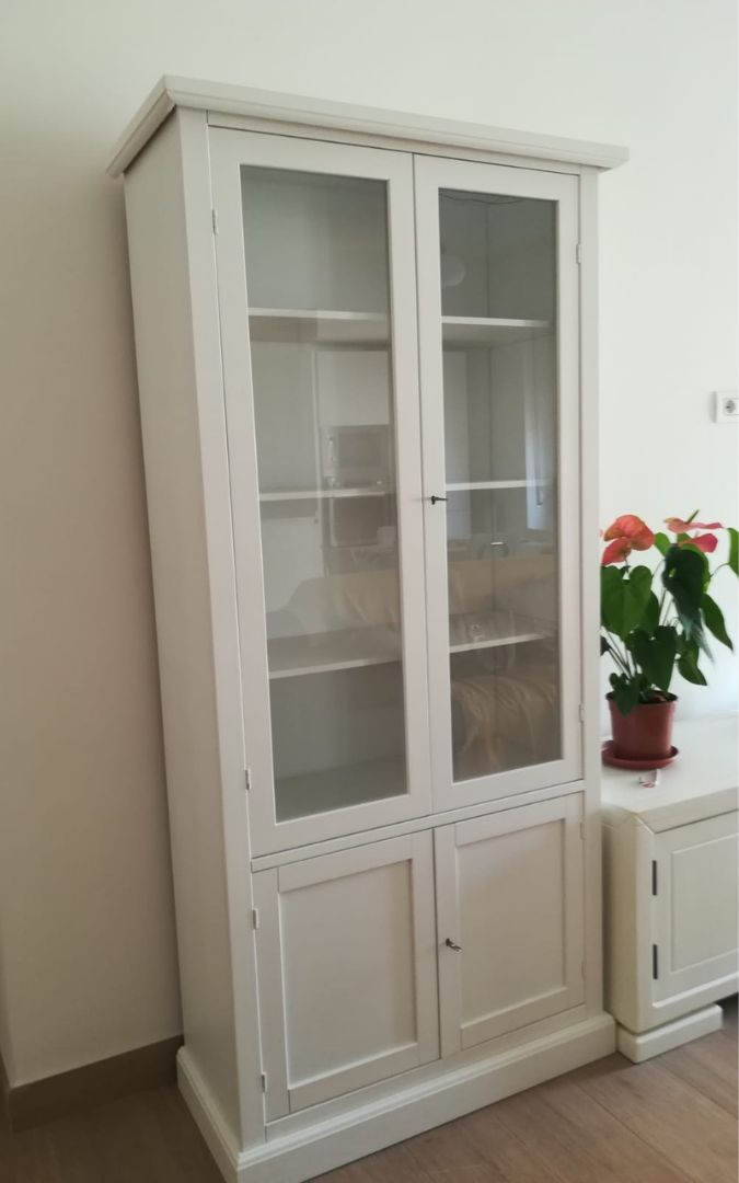 Vetrina libreria in legno bianco opaco riempita di libri, ideale per un ambiente studio o salotto.