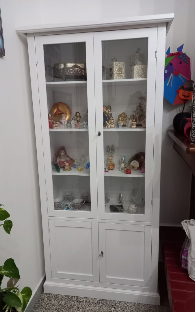 Vetrina classica bianca utilizzata come credenza per esporre servizi di piatti e porcellane.