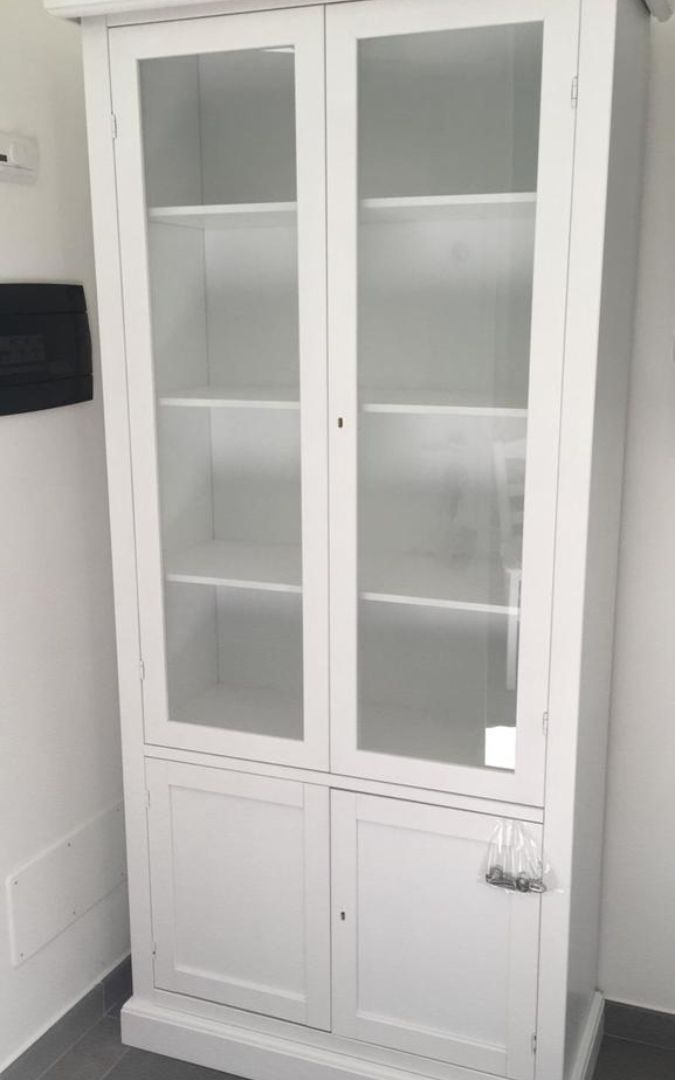 Vetrina in legno bianco opaco vista in negozio, ante a vetro e scomparto inferiore chiuso.
