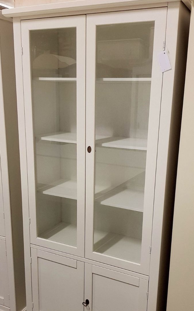 Vetrina in legno bianco opaco con cornice superiore, stile classico, posizionata in un soggiorno.