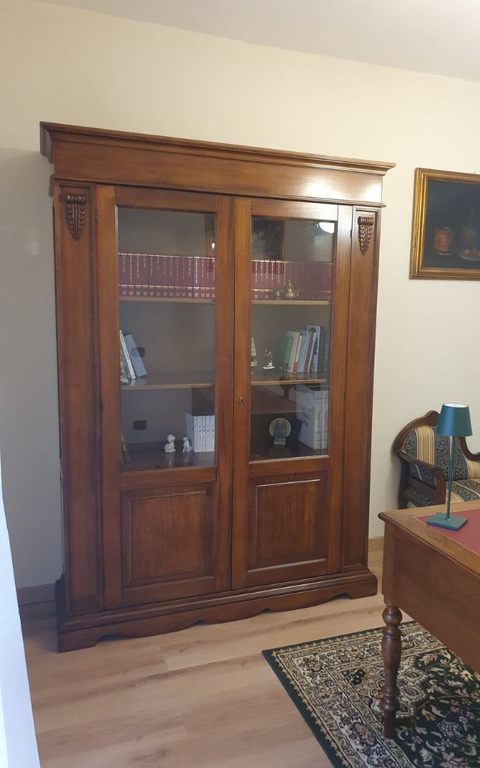Elegante vetrina in legno color noce scuro stile arte povera con due ante vetrate e ripiani interni a vista in un ufficio classico.