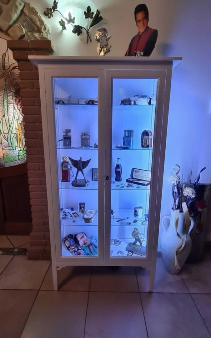 Vetrina in legno bianco opaco stile arte povera, illuminata, vista frontale completa.