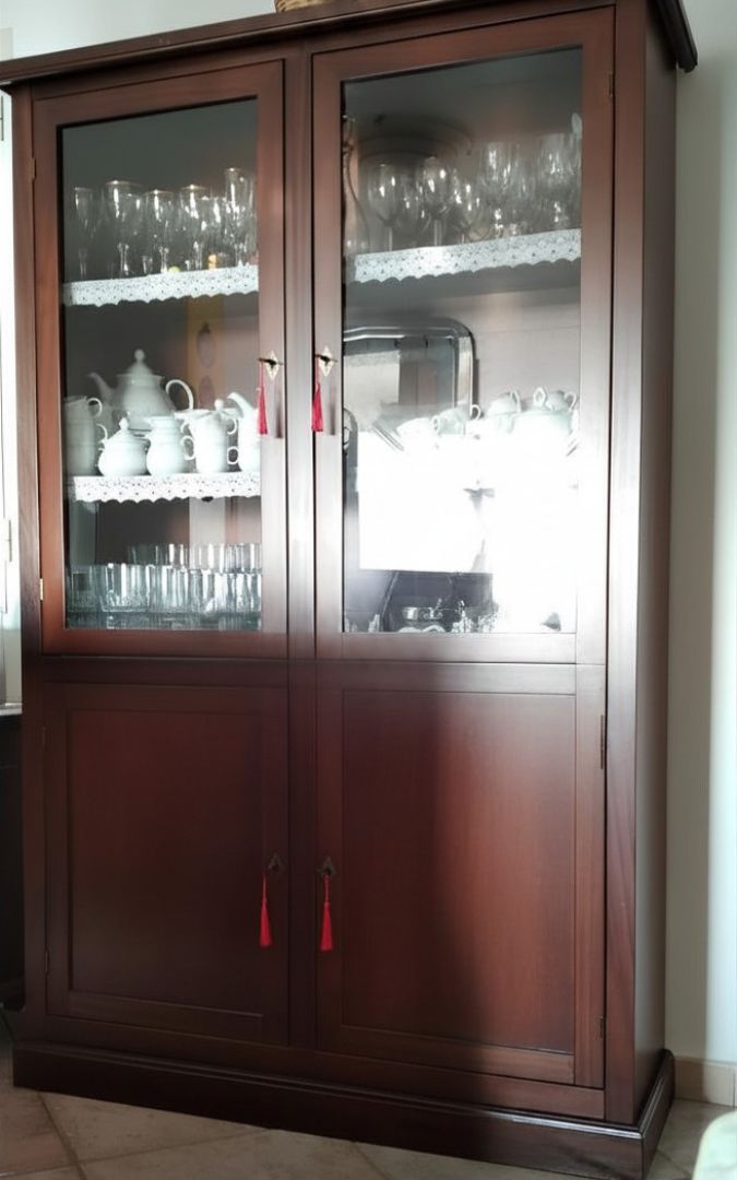 Dettaglio di vetrina in legno noce scuro con bicchieri e stoviglie esposti dietro ante in vetro.