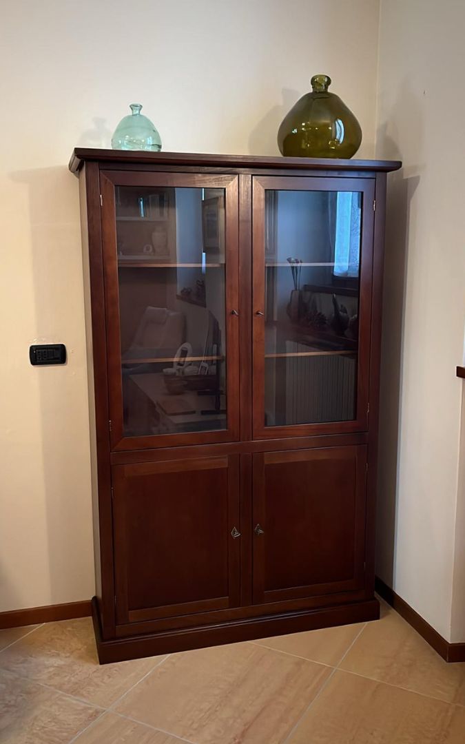 Vetrina in legno noce scuro arredata con decorazioni, con ante a vetro superiori e ante cieche inferiori.
