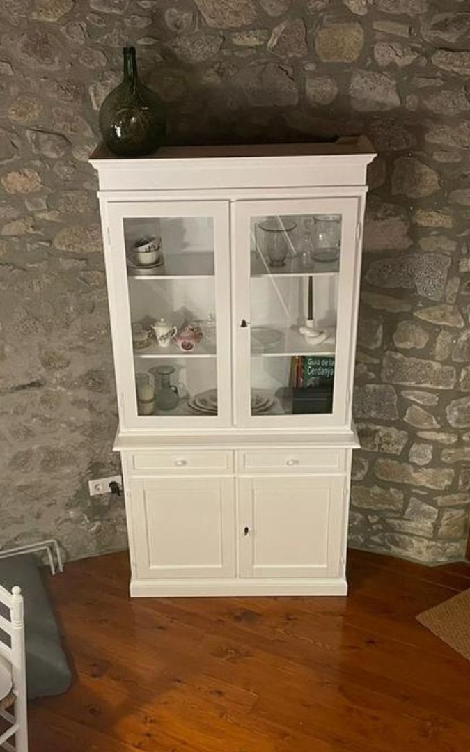 Vetrina in legno bianco opaco, vista frontale, con vani superiori vetrati e base chiusa a due cassetti.