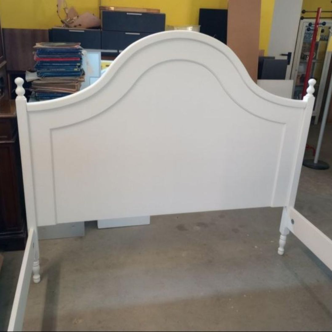 Letto matrimoniale in legno bianco stile classico con testiera sagomata e dettagli decorativi.