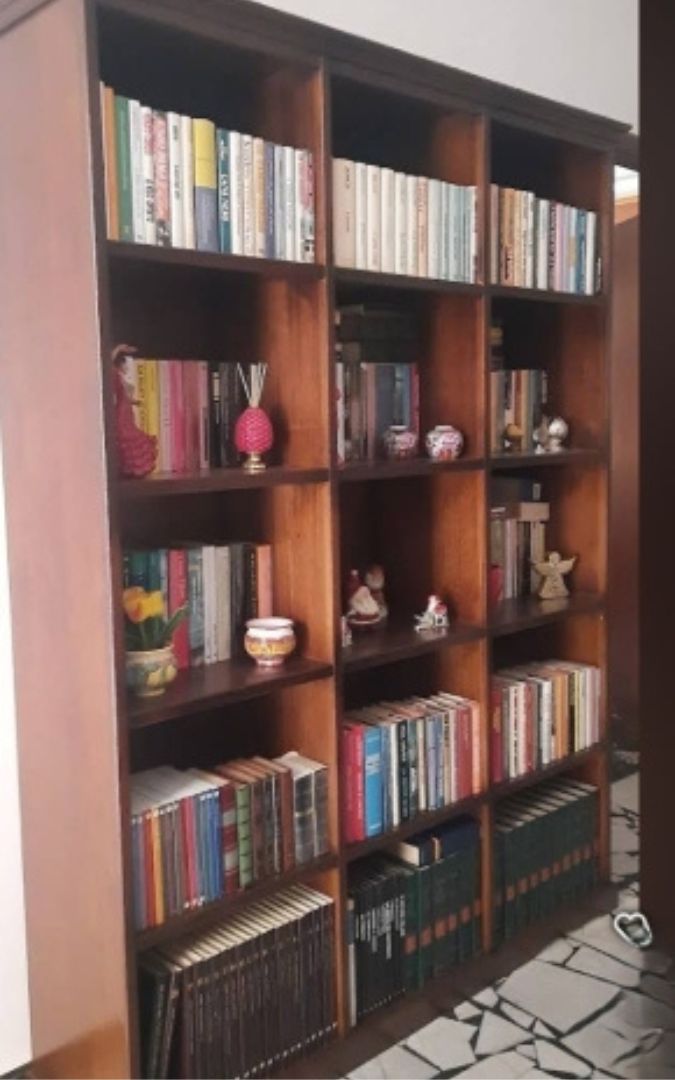 Ampia libreria a giorno in legno color noce scuro in stile arte povera, completa di numerosi libri e oggetti decorativi.