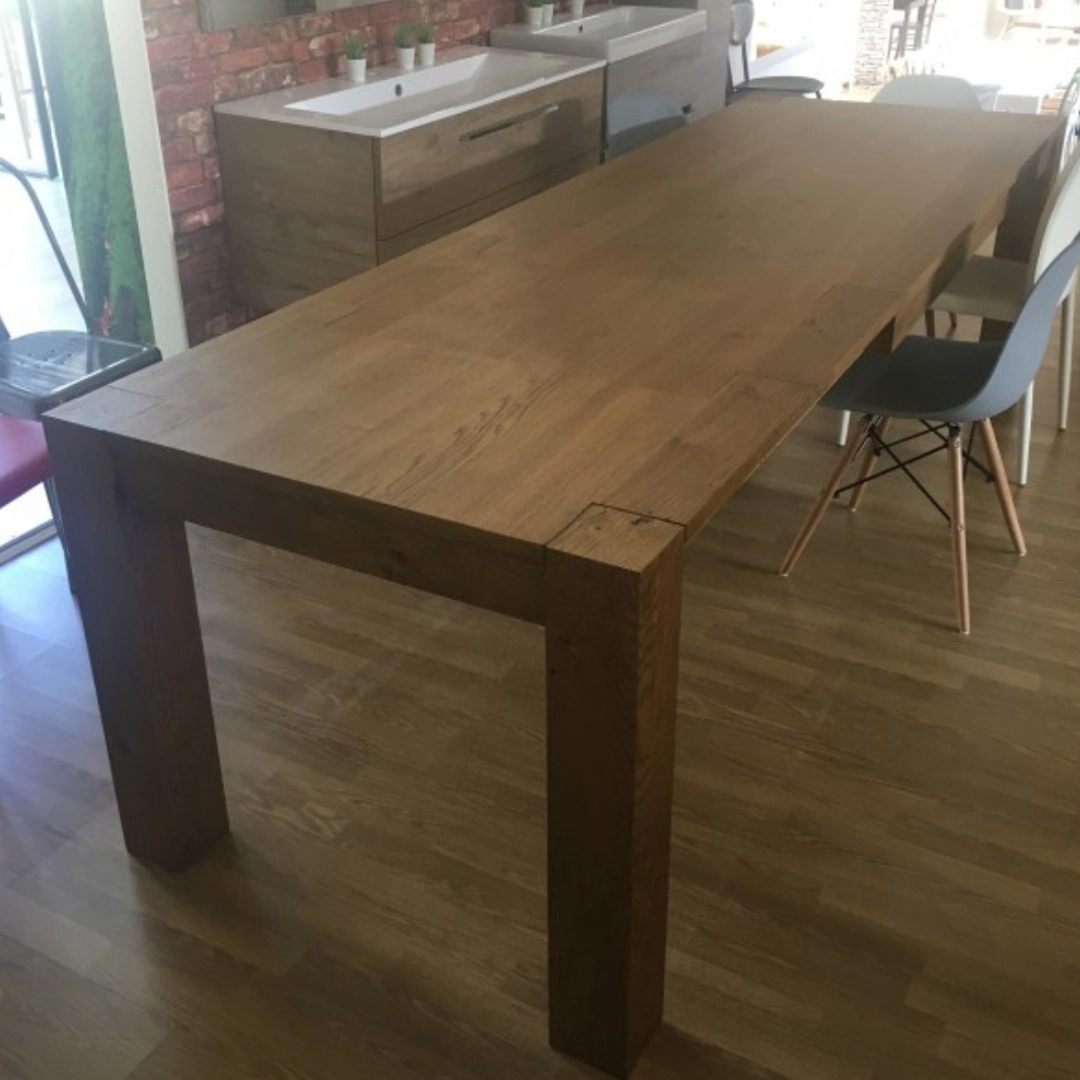 Il grande tavolo da pranzo in rovere Marca Design Shop con gambe possenti, visto in un'ambientazione luminosa vicino a un mobile da bagno in legno.