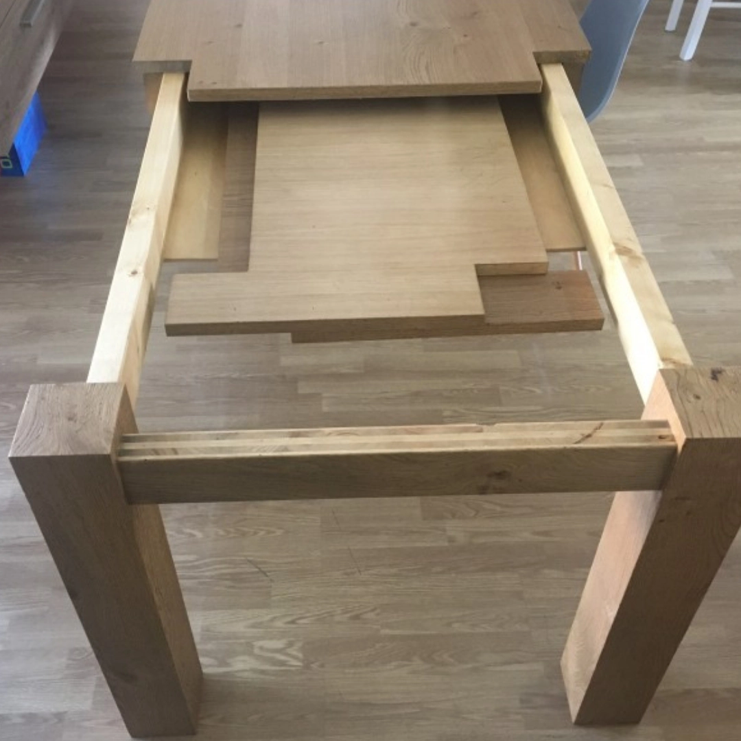 Inquadratura dall'alto dell'apertura a libro del tavolo Marca Design Shop, che mostra il sistema di scorrimento e le prolunghe in rovere riposte all'interno.